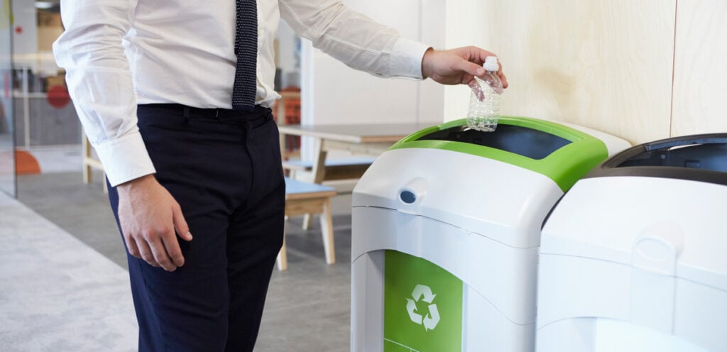 Man in shirt and tie putting PET bottle into a recycling bin