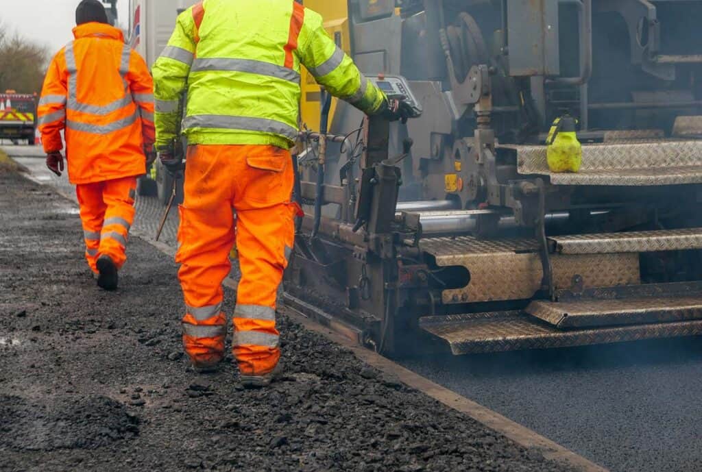 construction workers carrying our roadworks laying new asphalt stock photo